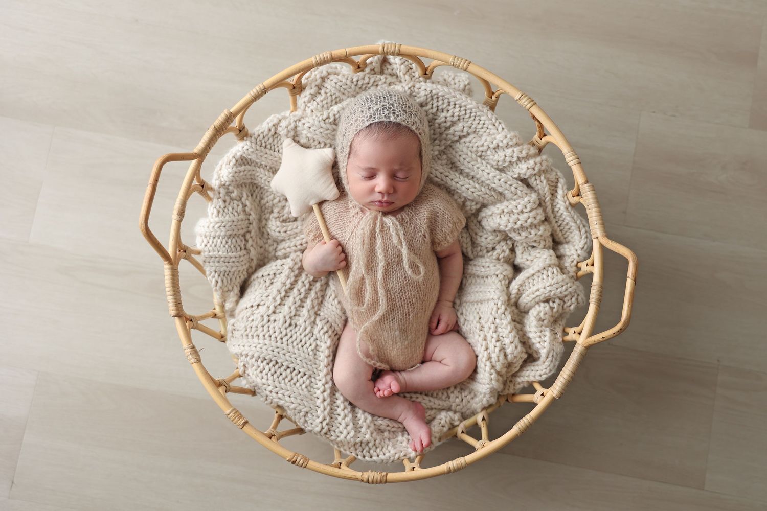 Whimsical newborn studio portrait of a sleeping baby holding a felt star wand inside a round rattan basket