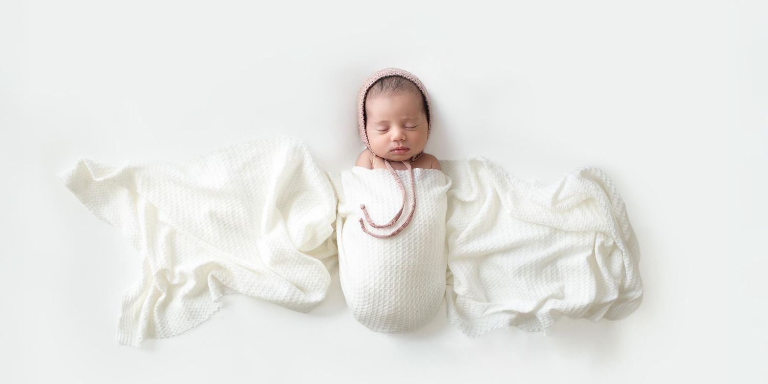angelic sleeping newborn wearing pink bonnet covered with white flowing blanket