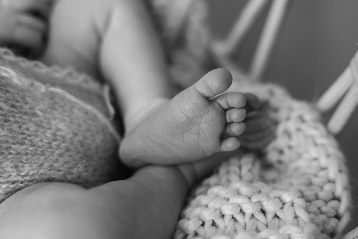 Black and white macro photography detail shot of tiny newborn baby toes resting on a chunky knit blanket