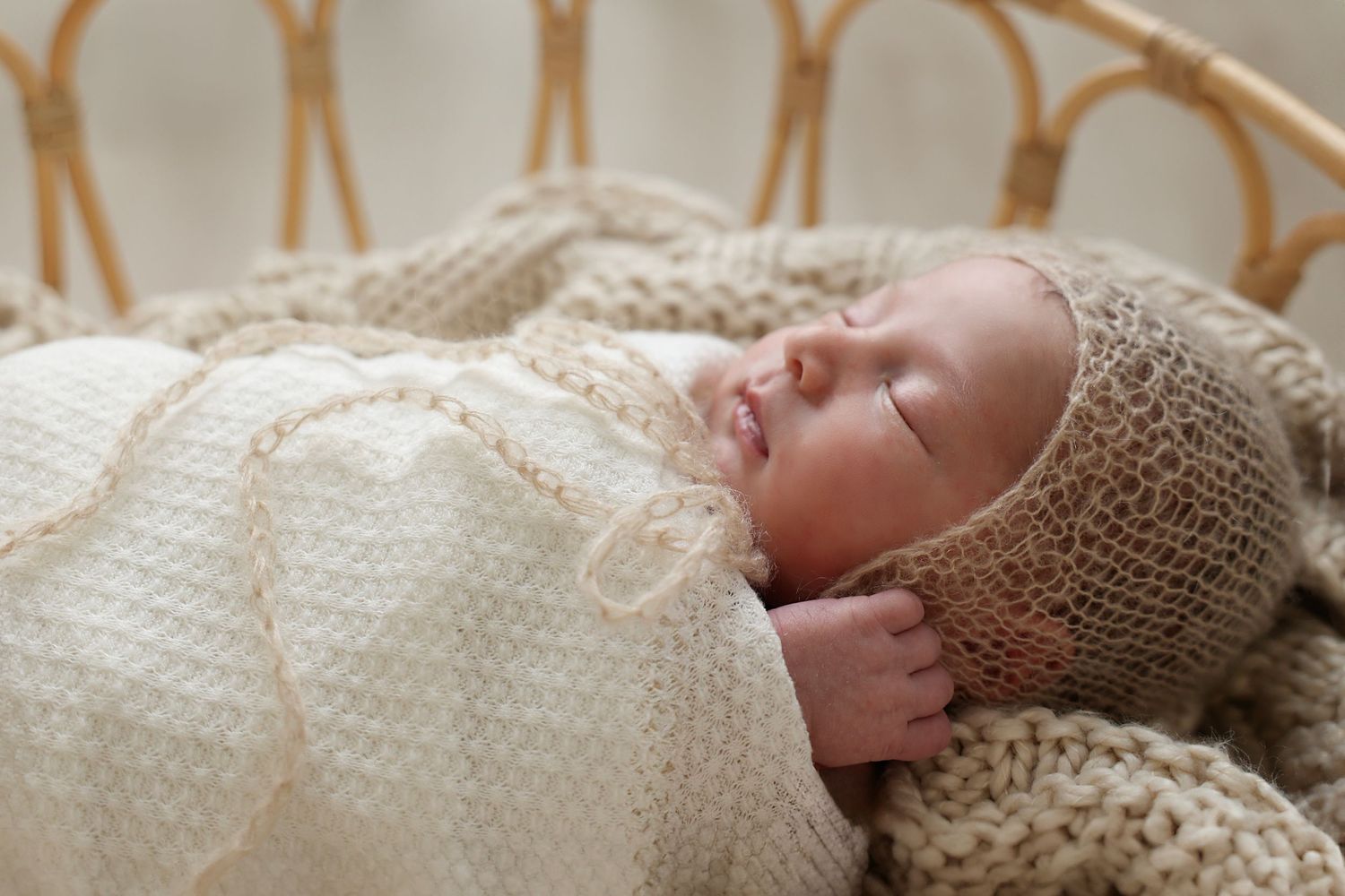 A sleeping newborn wrapped in a soft knitted blanket and hat, peacefully nestled in a woven basket.