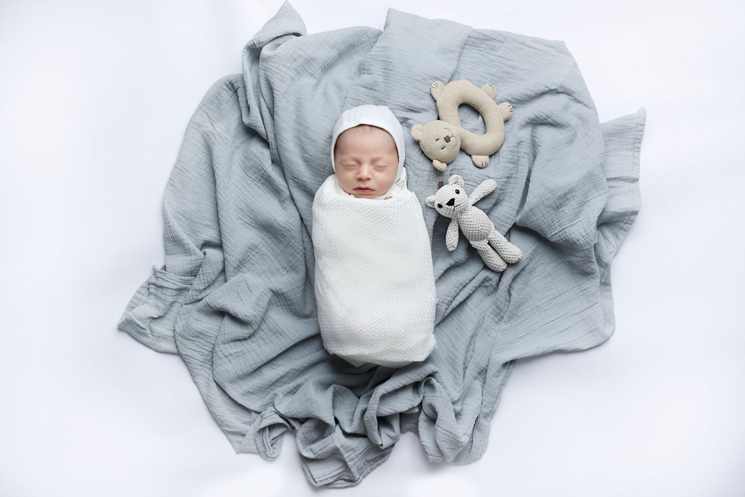 Newborn swaddled in white blanket lying onto of a soft blue blanket with knit toy nearby