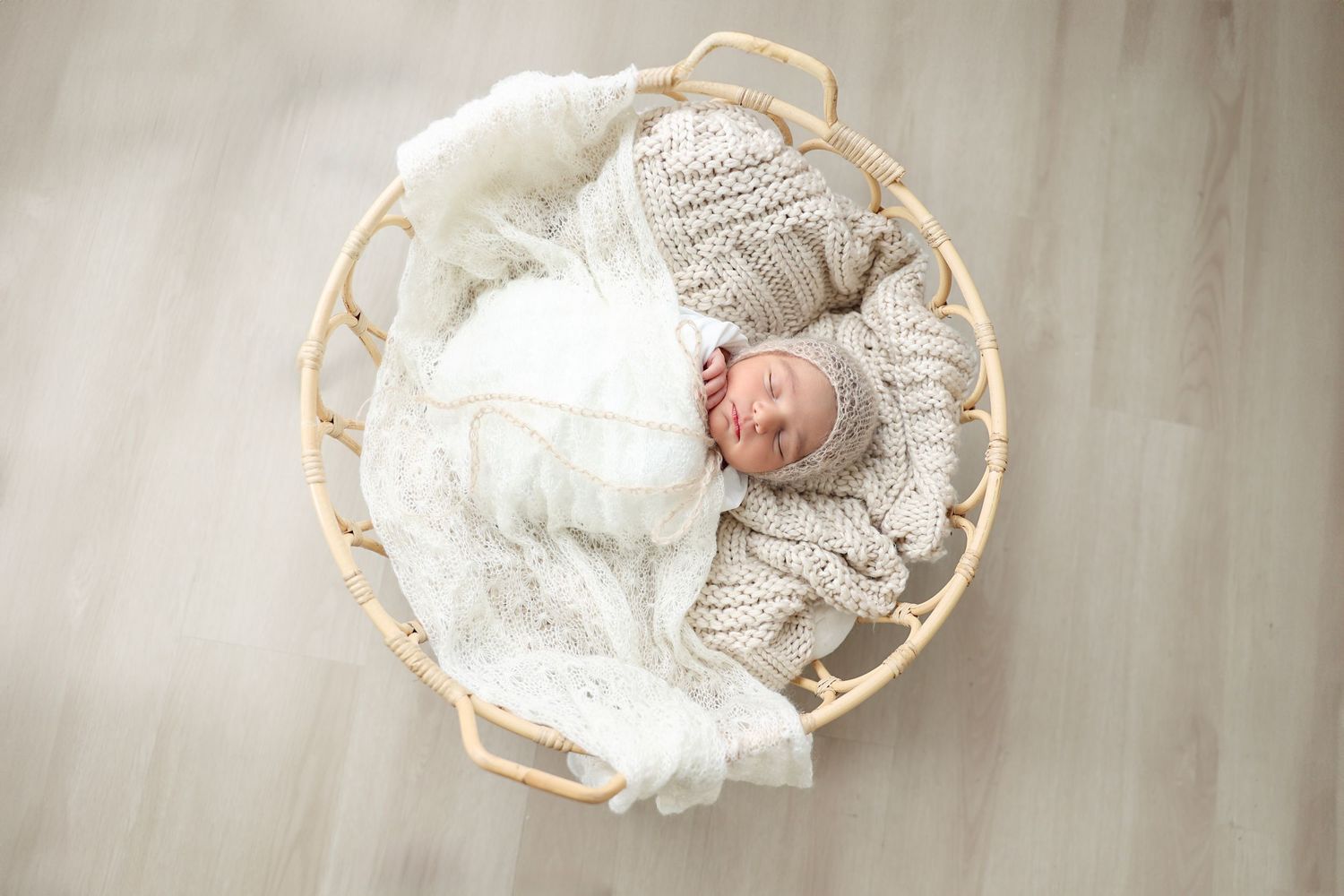 A sleeping newborn wrapped in a soft, beige knitted blanket and hat, peacefully nestled in a woven basket, creating a serene atmosphere.