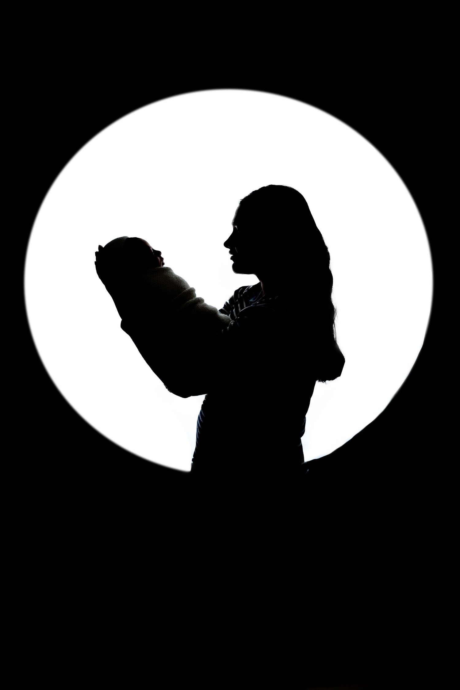 Dramatic silhouette of a mother holding her newborn baby against a bright white circular  background