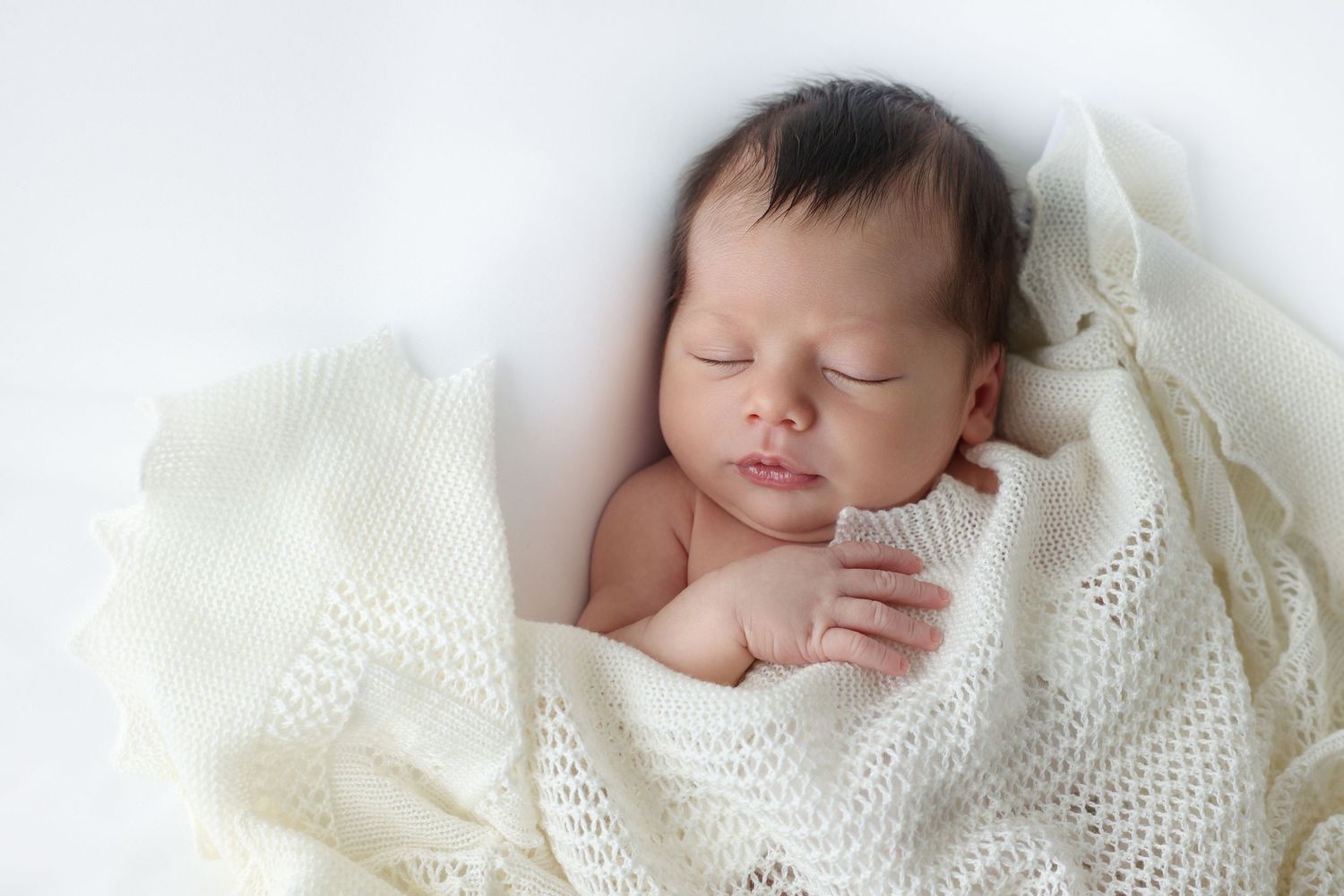 Classic white-on-white newborn photography featuring a sleeping infant covered in a vintage-style crochet blanket