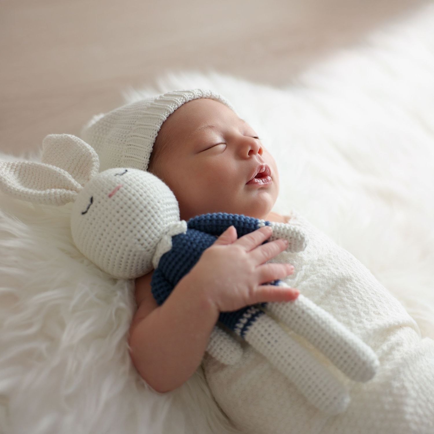 Heirloom-style newborn photography featuring an infant holding a handmade knit rabbit doll on a soft white fur background