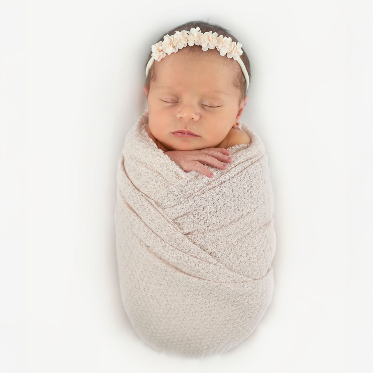 Classic potato sack pose of a sleeping newborn baby girl tightly swaddled in a textured wrap on a white background