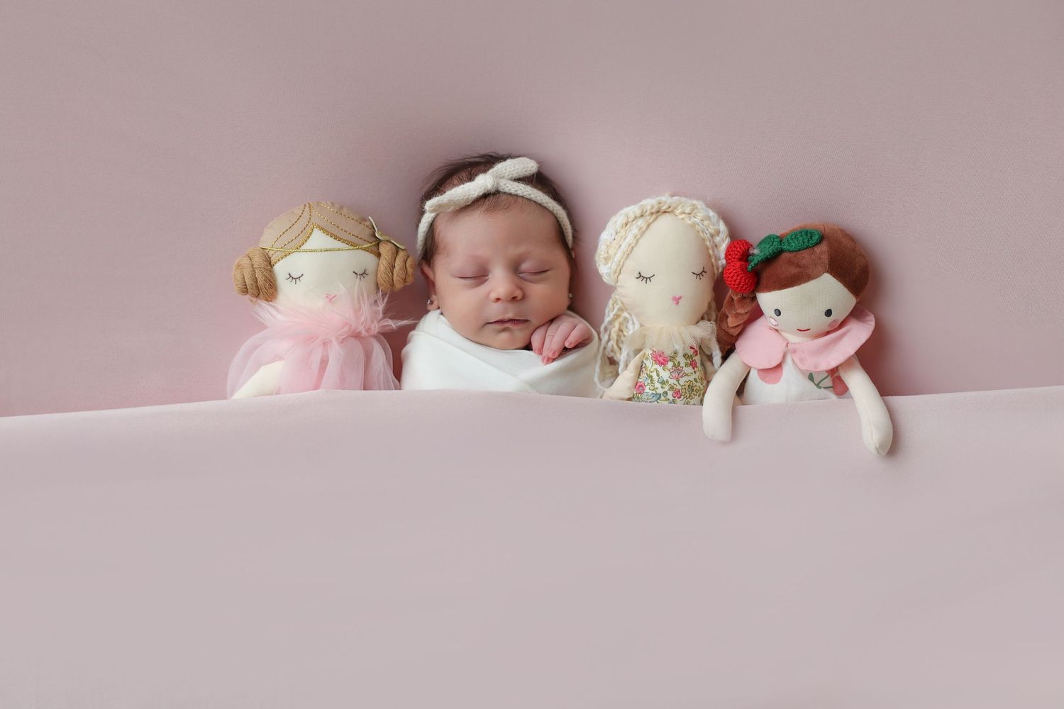 adorable image of newborn girl wearing a knit bow snuggled near pretty dolls