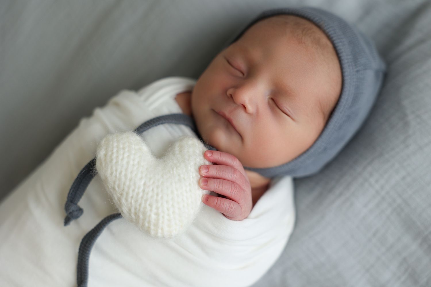 close up image of an angelic newborn holding a soft, knit, white heart in his little fingers