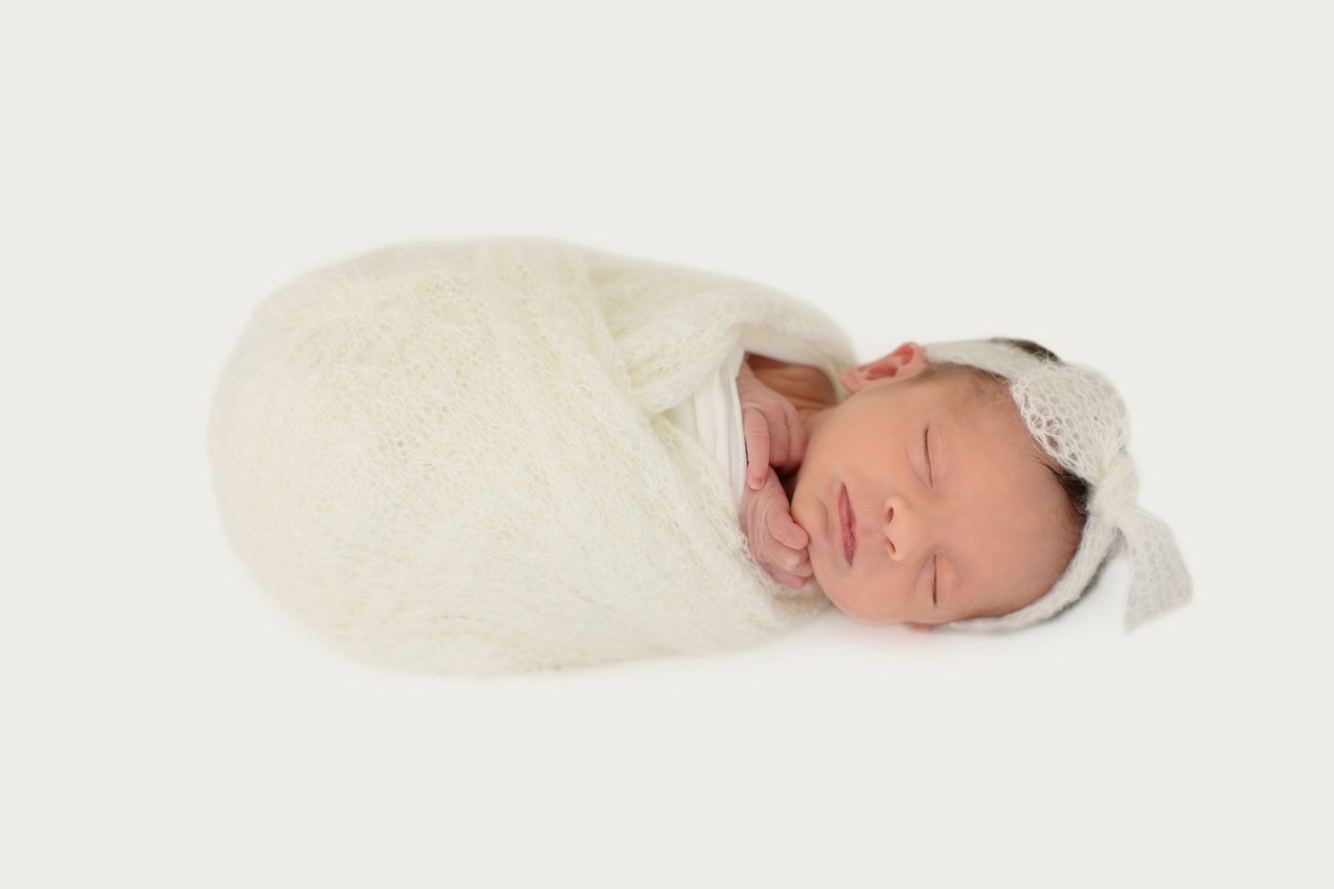 dreamy newborn baby in a soft, knit swaddle with matching headband bow