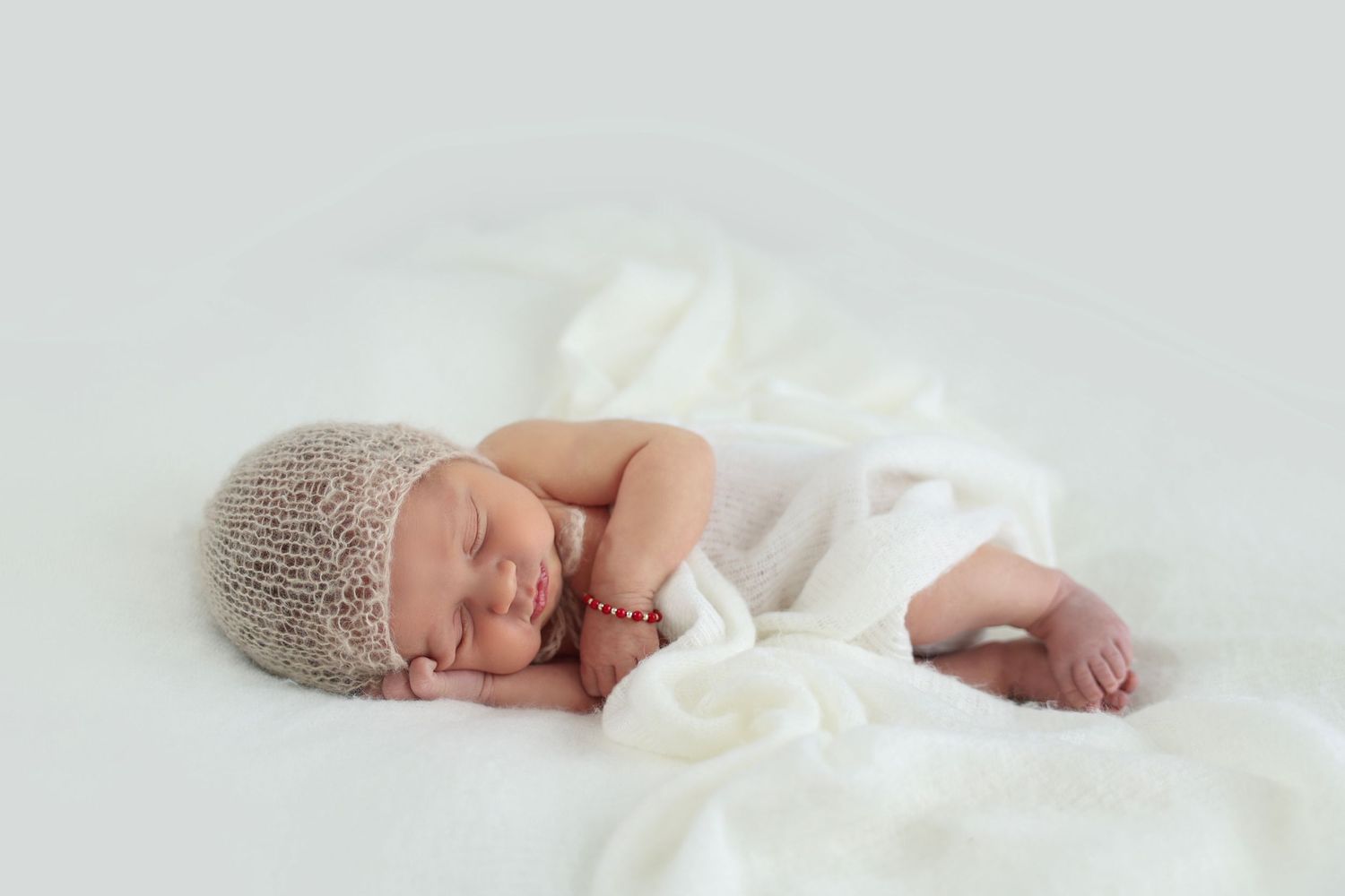 A sleeping newborn with a soft knitted hat resting her cheek on her hand
