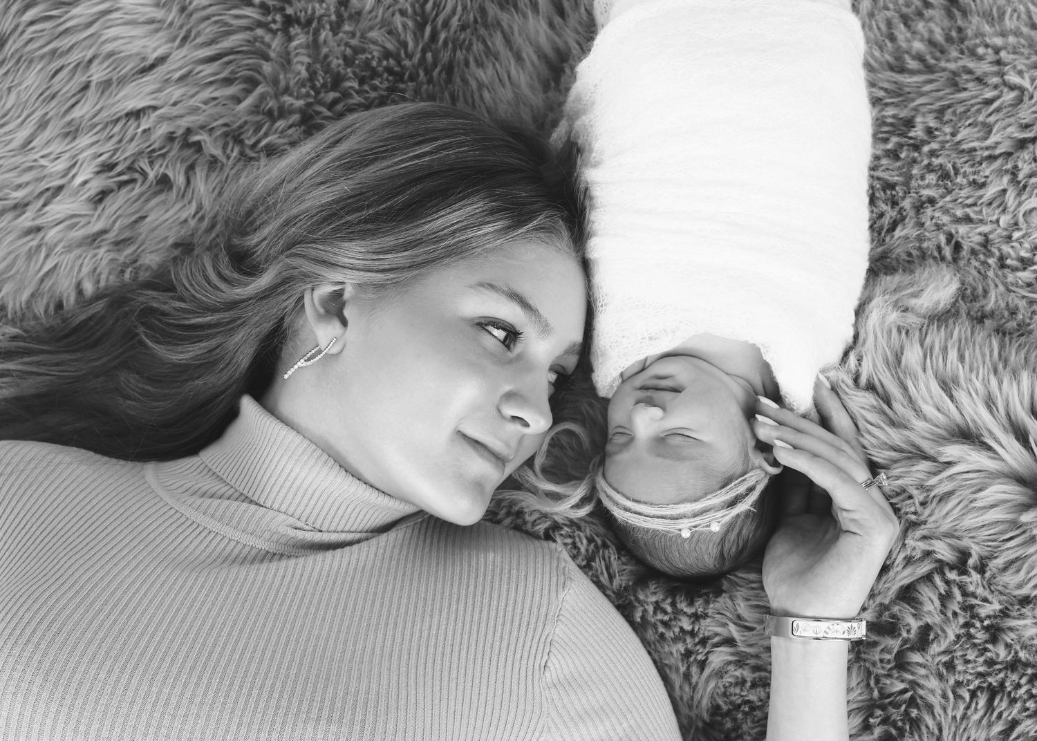 portrait of mom and swaddled, sleeping newborn cuddled on a textured rug