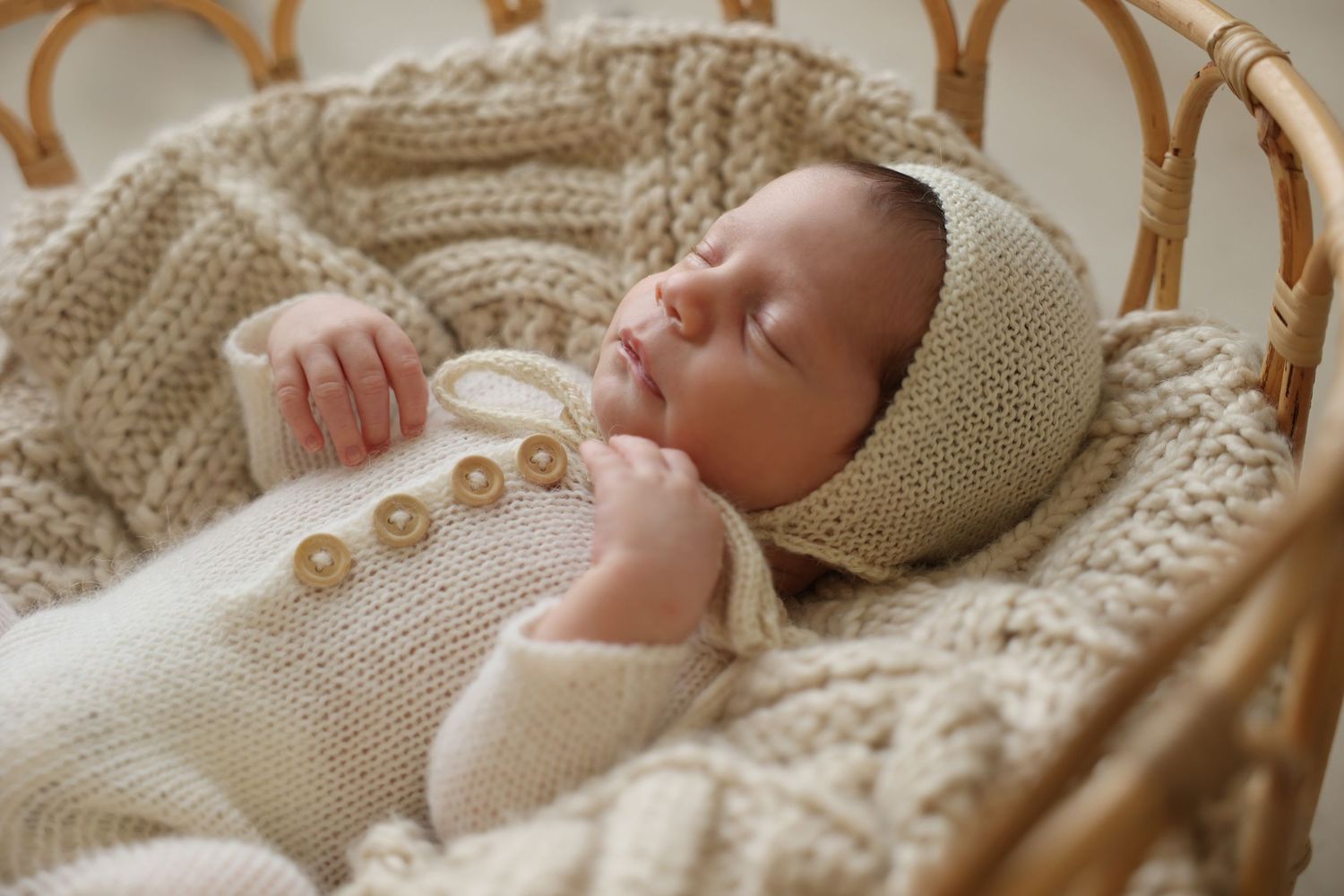 Sleeping newborn baby lying in a vintage-style rattan basket filled with a chunky cream knit blanket