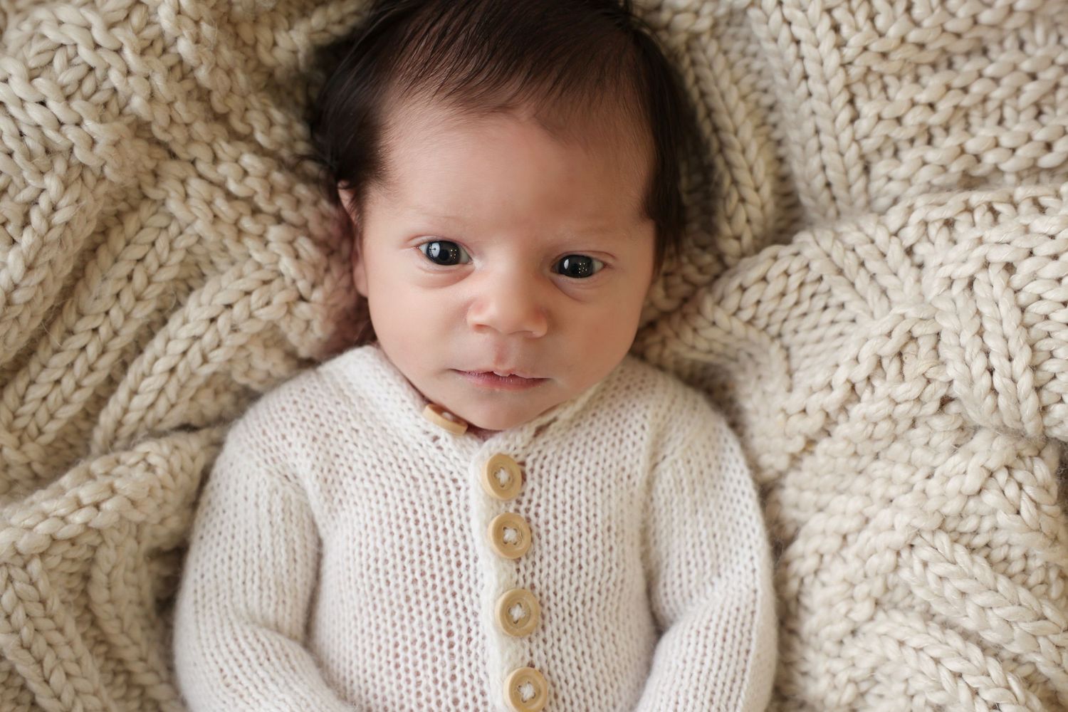 Beautiful awake newborn photography shot featuring a baby with dark hair making direct eye contact with the camera