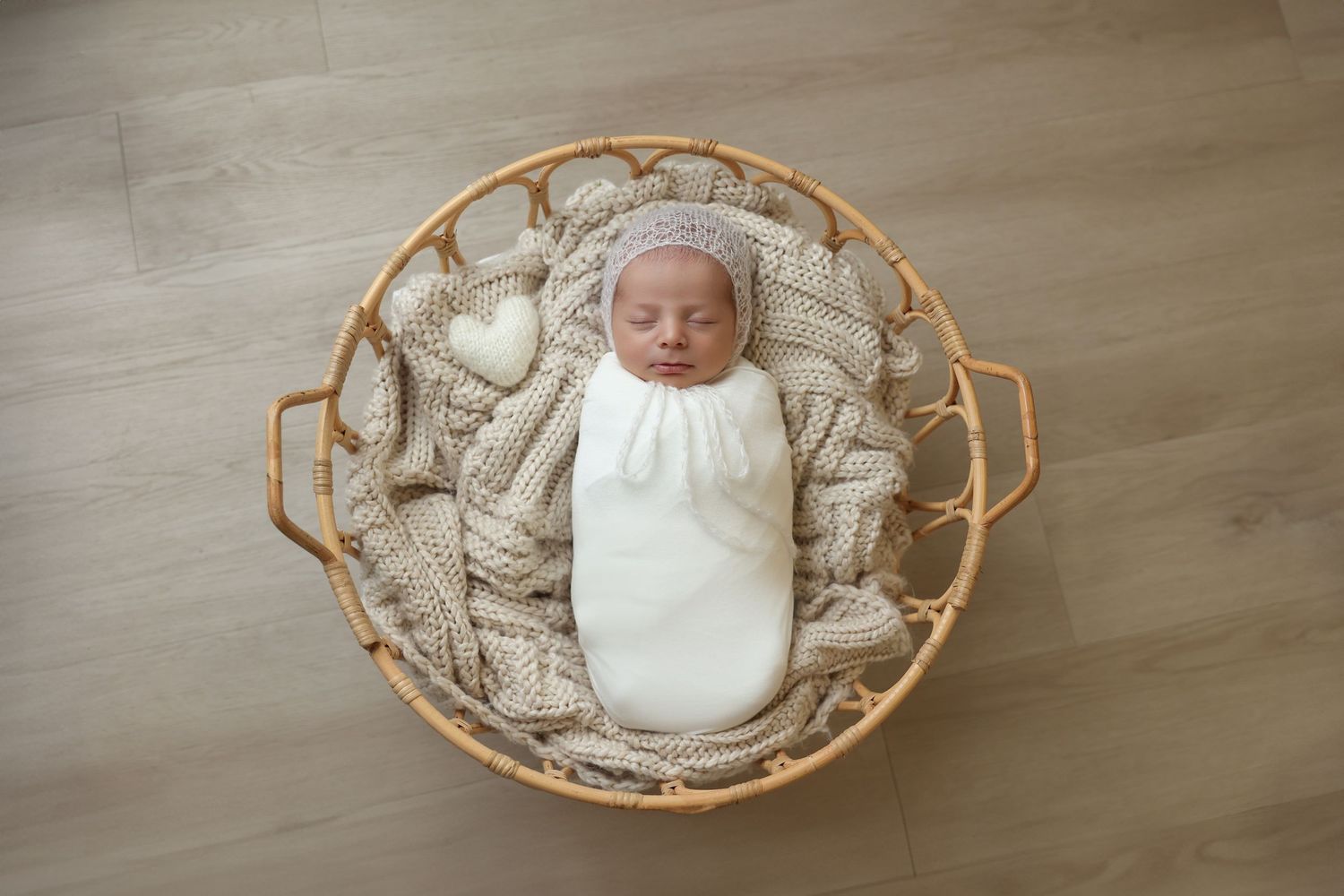 A peaceful newborn baby sleeping in a woven basket, wrapped snugly in a white swaddle