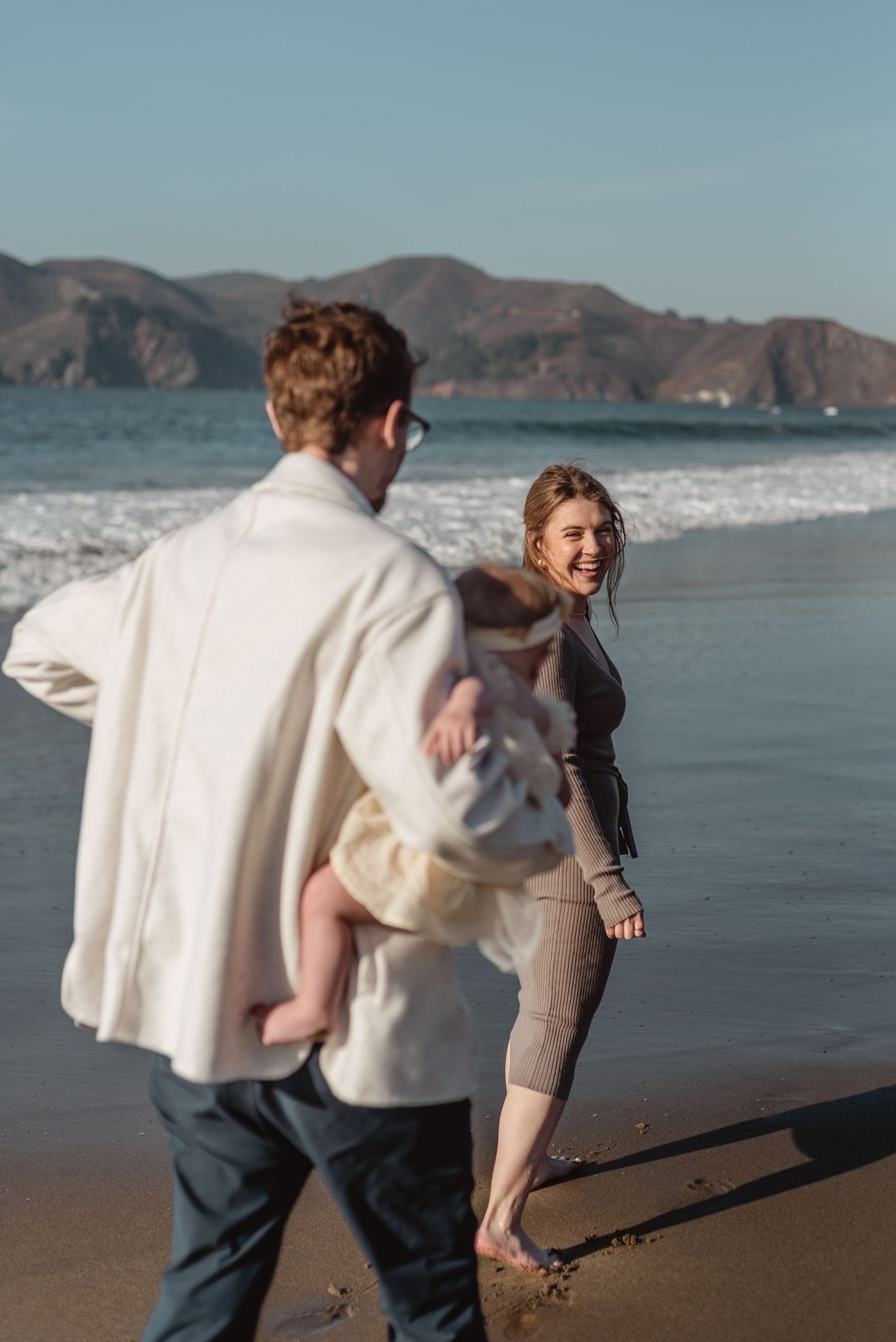 Couple enjoying a beach walk with mountains and waves in the background.