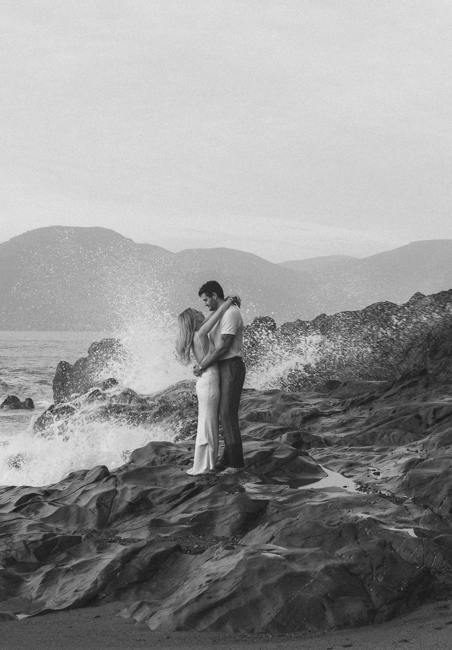 Waves crash against rocky coastal cliffs as figures stand in silhouette.