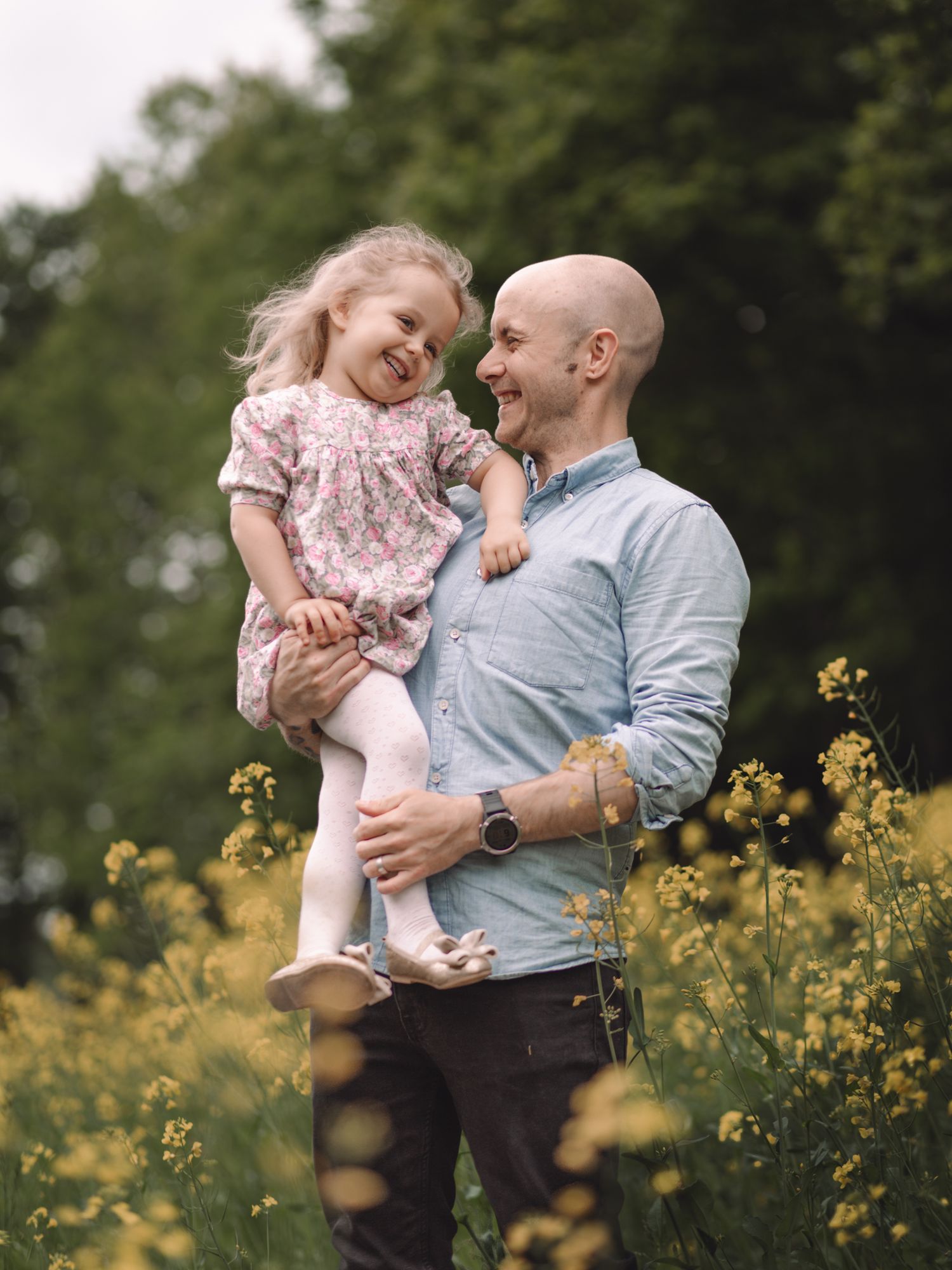 Sweet candid moment between parent and child laughing together in a field of yellow flowers.
