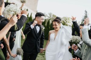 Wedding party laughs together during outdoor celebration in garden setting.