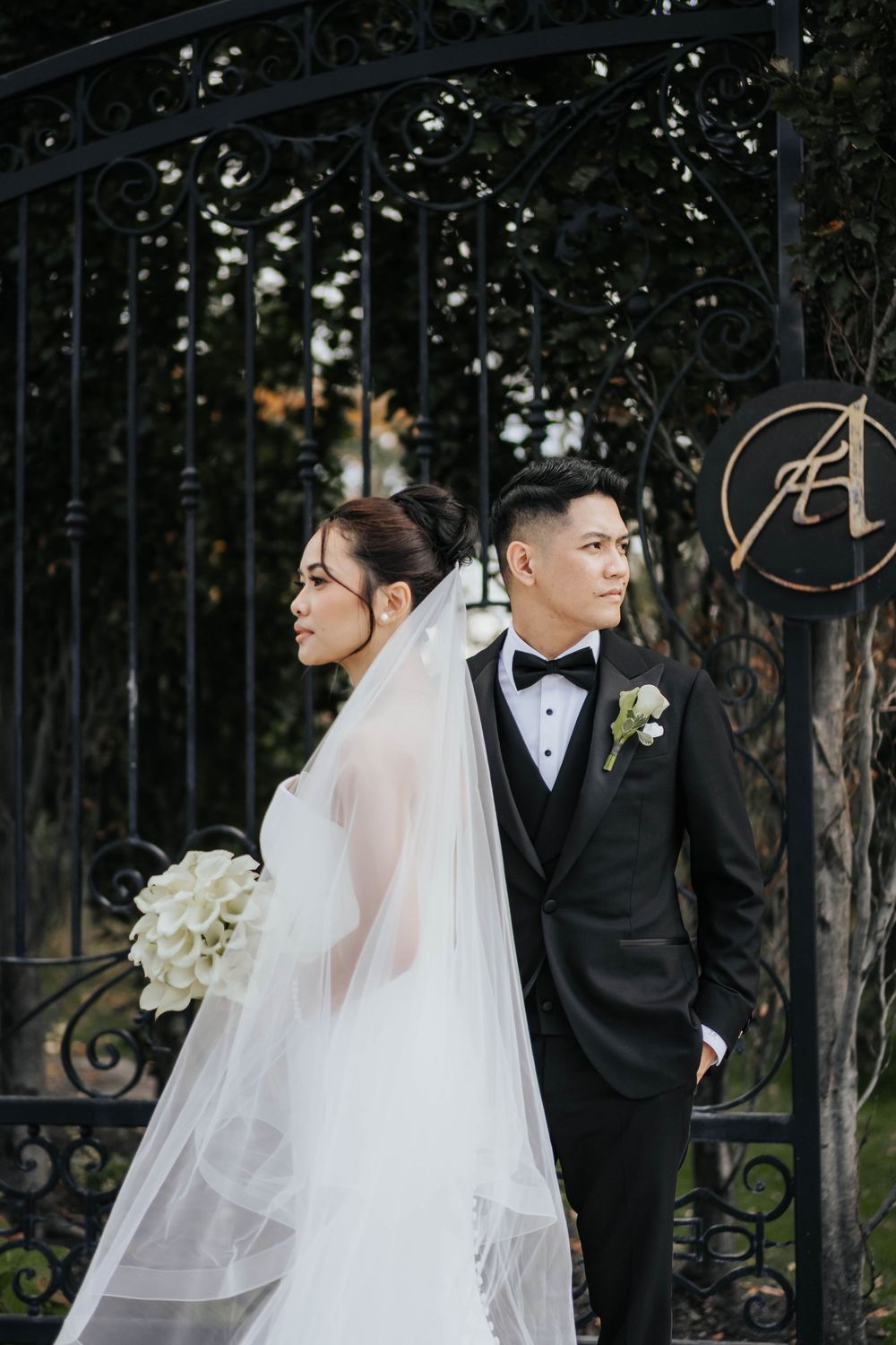 Bride and groom share intimate moments in elegant outdoor wedding photos with white floral details and iron gates.