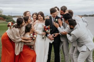Wedding party shares joyful moment together outdoors while wearing orange and neutral colored attire.
