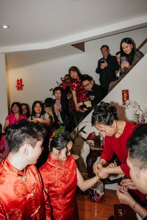 A group of wedding guests in red traditional Chinese attire dance and celebrate together at an indoor reception party.