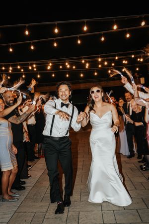 Wedding guests dance and celebrate under warm string lights on an outdoor patio during an evening reception.