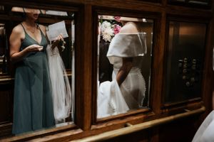 Reflective wedding scene captured through vintage wooden window panes showing dress preparations.
