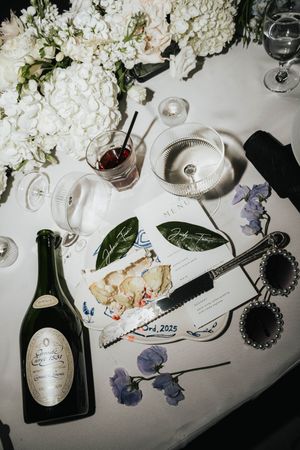 Elegant table setting with Dom Perignon champagne bottle, white flowers, and handwritten notes on a white tablecloth.