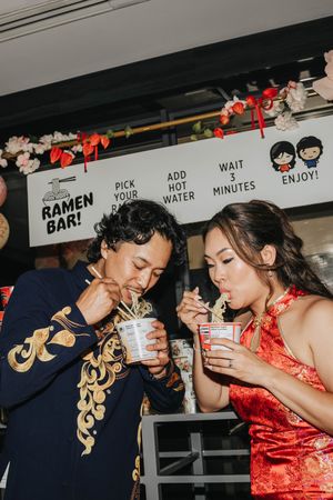 Couple enjoying instant ramen together at a casual dining counter with instructional signage visible in background.