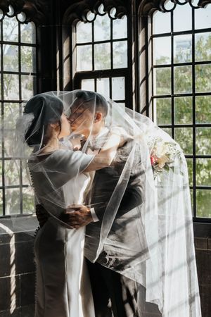 Intimate wedding moment captured through a delicate veil by gothic windows.