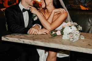 A couple sits at a rustic wooden table during their wedding reception, sharing an intimate moment together.