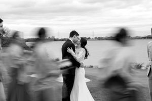 Artistic black and white photo of newlyweds embracing while guests create motion blur around them.