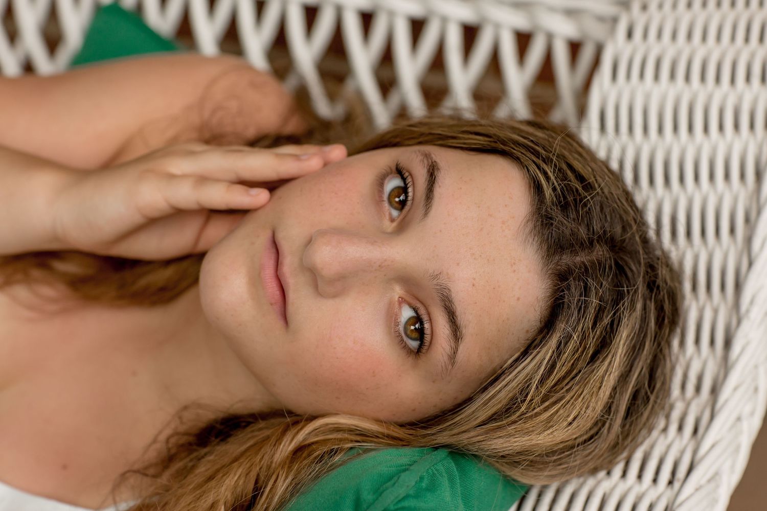 Young woman with brown hair lying in white wicker chair looking up.