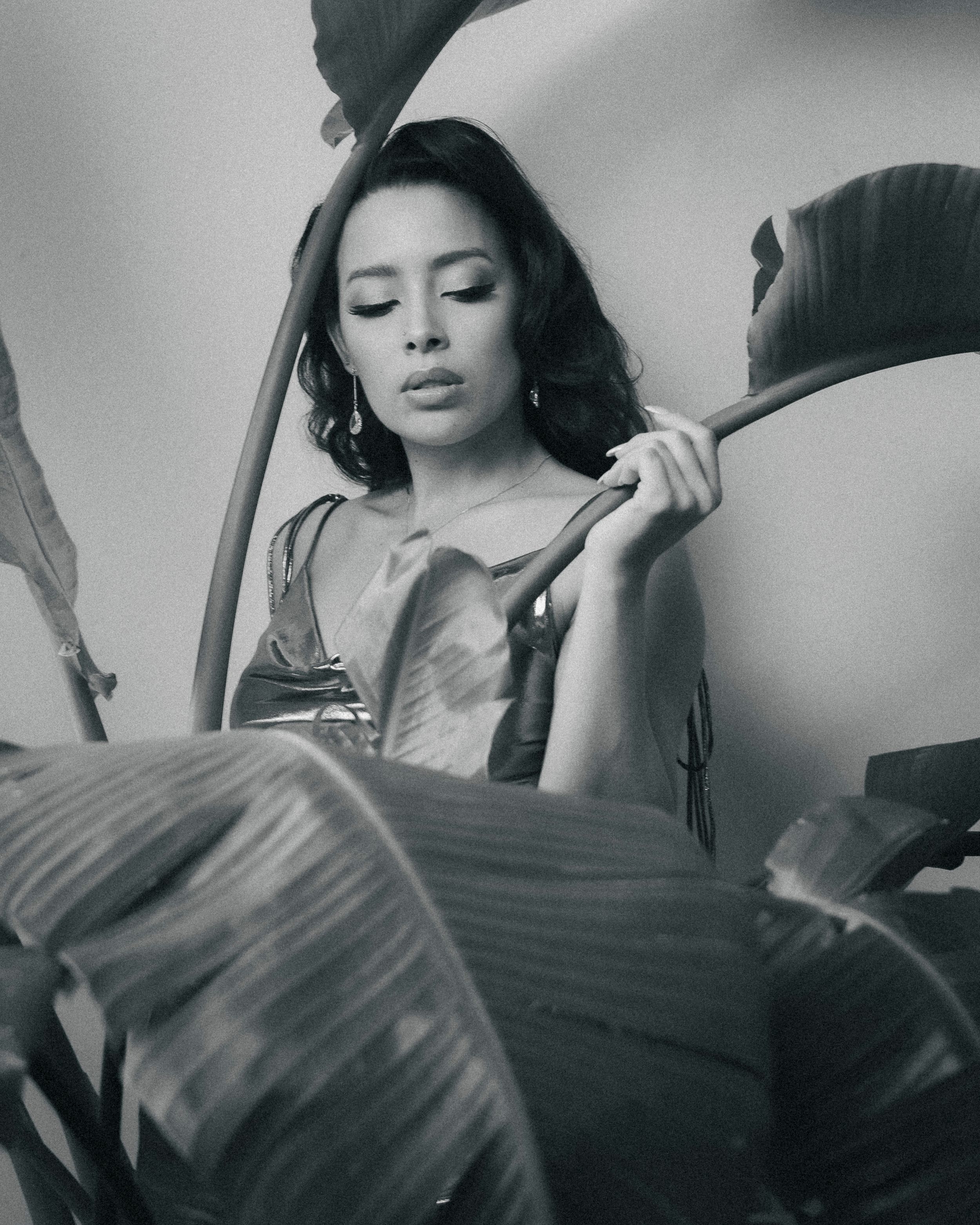 A black and white portrait of a woman posing elegantly among tropical leaves.
