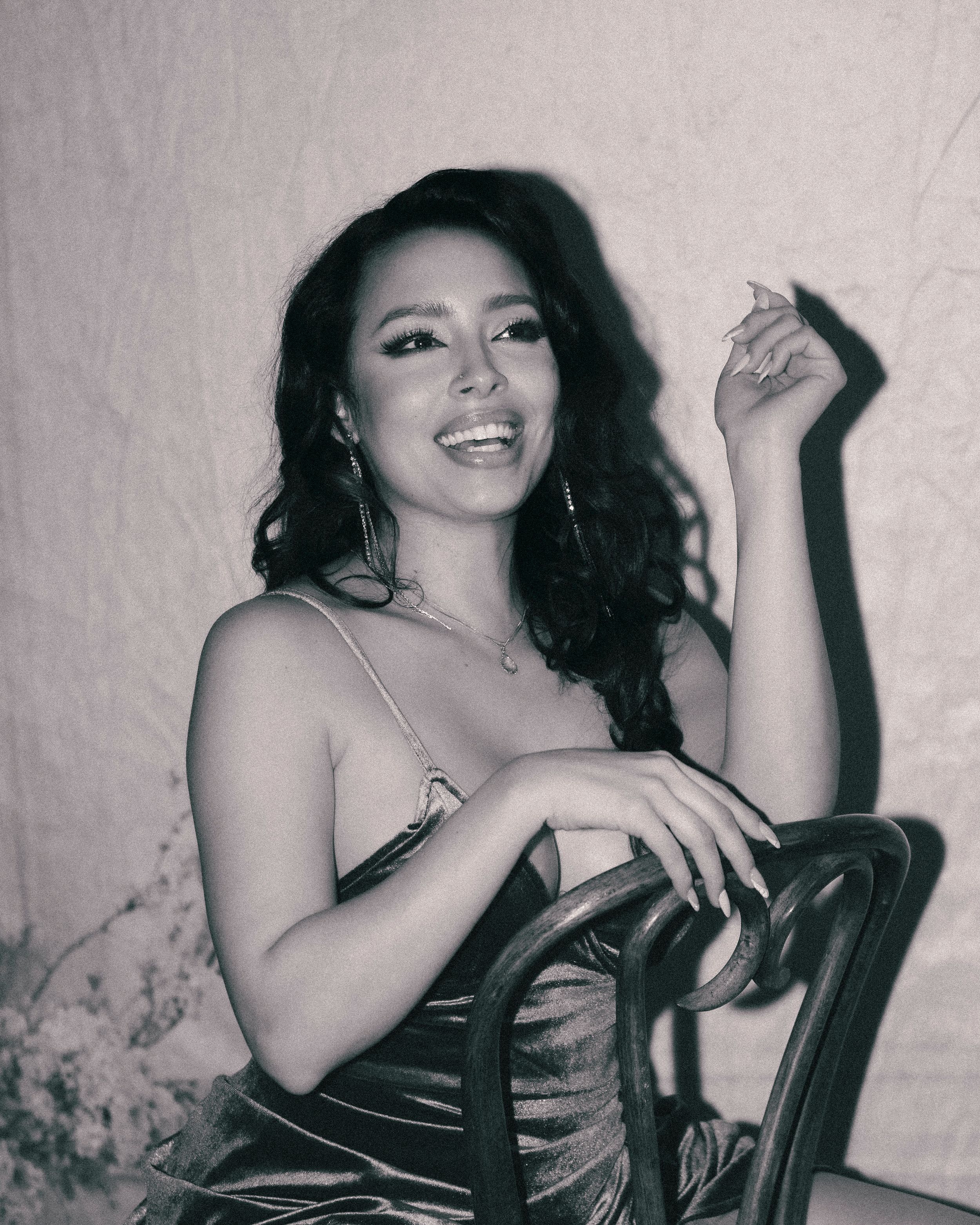 Vintage-style portrait in corset with wavy hair and relaxed pose on chair.