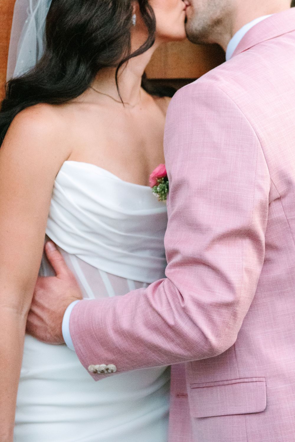 Close-up of a bride in white dress and groom in pink suit sharing an intimate moment.