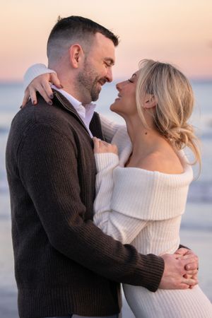 Romantic beach photoshoot at sunset with couple in casual winter attire.