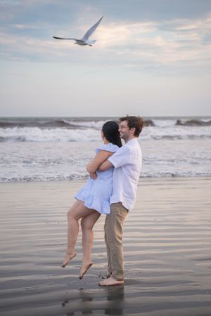 Couple embracing on a misty beach at sunset with waves crashing in the background.