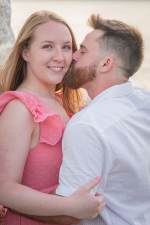 Tender moment between couple in pink and white outfits during sunset photoshoot.
