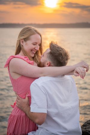 Couple laughing and embracing against golden sunset over water.