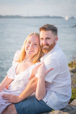 Couple cuddling on beach during golden hour with ocean in background.