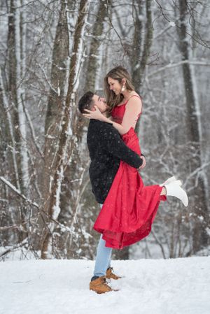 Couple in winter scene with red dress dancing in snowy forest.