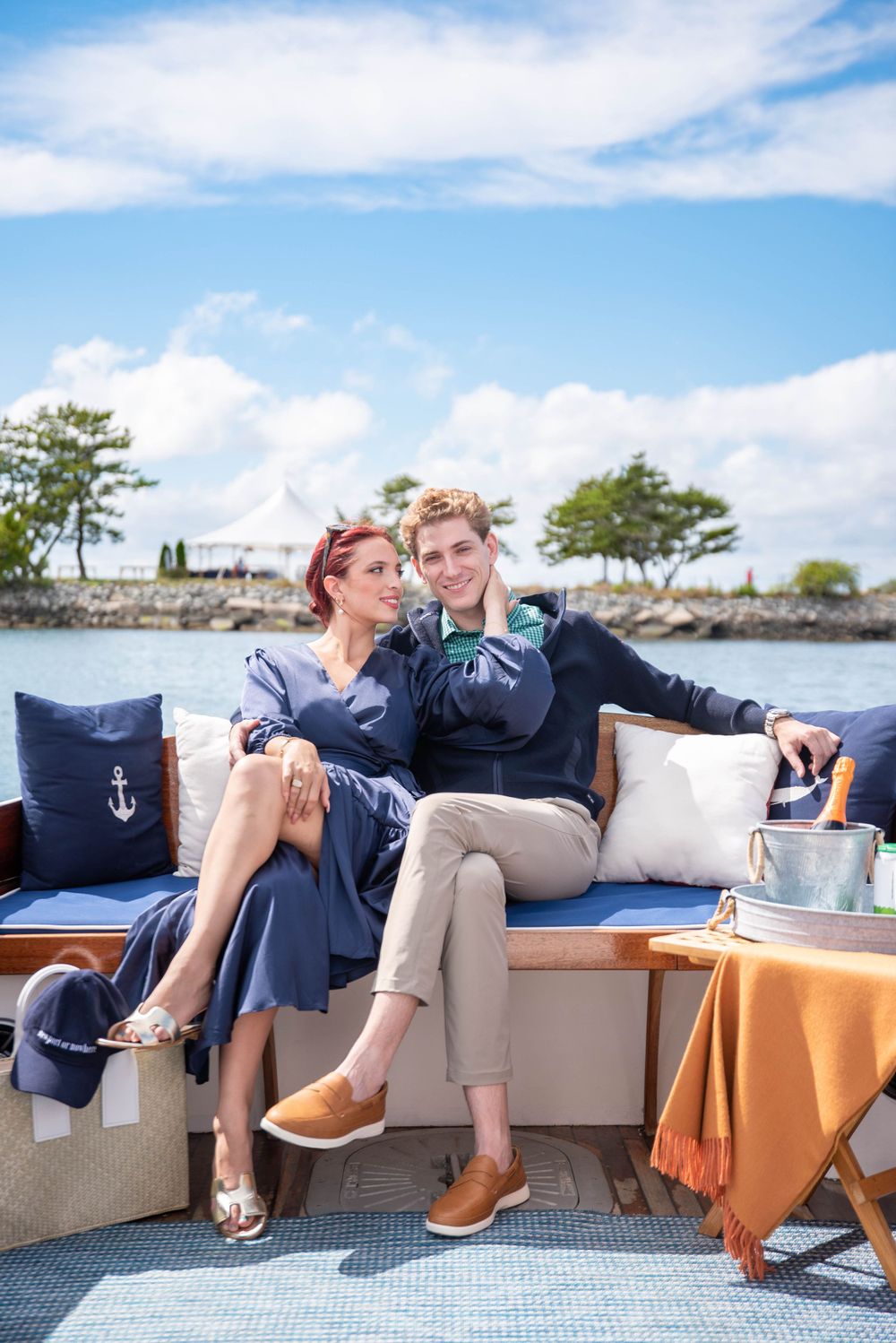 Couple lounging on cushioned boat seating with orange blanket and nautical decor.