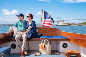 A couple relaxes on a wooden boat with an American flag waving in the coastal breeze.