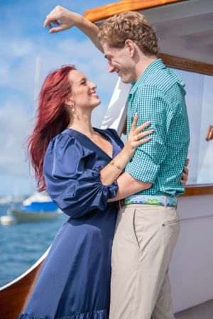 A romantic couple shares an intimate moment on a boat deck with the woman in a blue dress and man in checkered shirt.