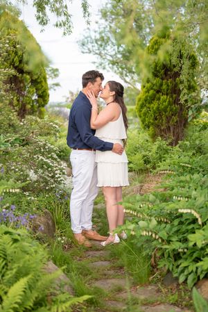 Romantic engagement photos in lush garden setting with white dress and navy outfit.