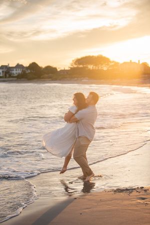 Joyful couple playing in ocean waves during golden hour sunset on sandy beach.