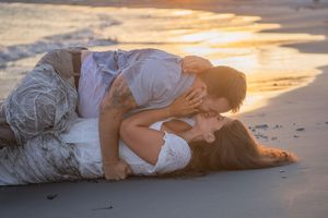 Romantic beach sunset photo with couple laying in sand as golden light streams across the ocean.