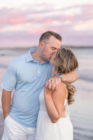A tender beach moment captured at sunset with soft pink clouds in the background.
