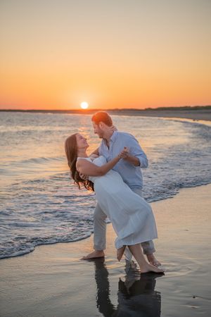 A romantic couple dances and embraces at the beach during golden hour.
